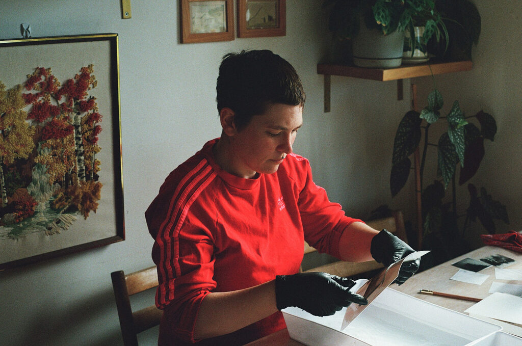 A photo of a woman holding a small paper over a plastic container of water. I the process of making polaroid emulsion lifts.
